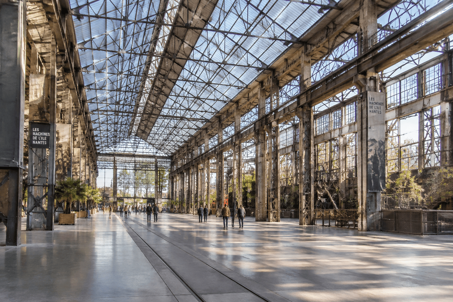 Vue d’une vaste halle aux charpentes métalliques et verrières, avec des panneaux indiquant Les Machines de l’île à Nantes.