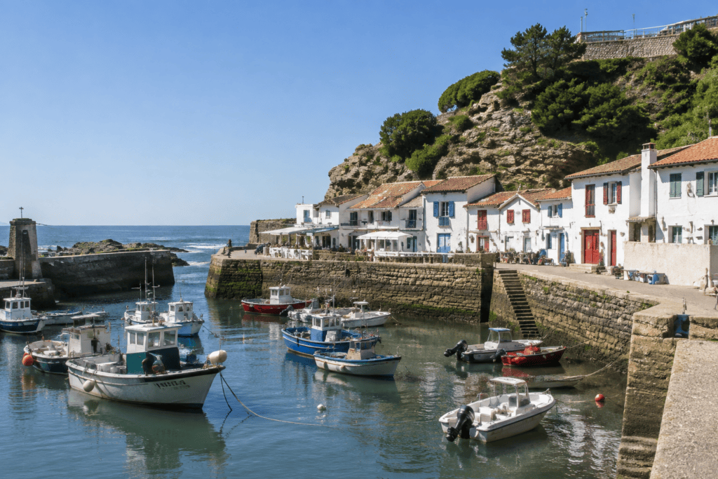 Petits bateaux amarrés dans un bassin bordé de maisons blanches aux volets colorés, au pied d’un versant rocheux.