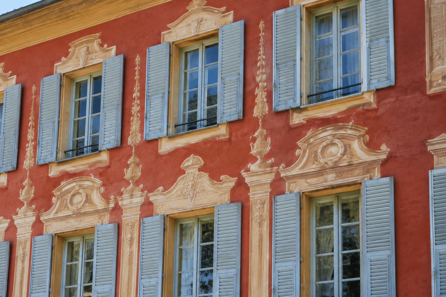 Façade rouge ornée de décors peints autour de fenêtres à volets bleus.