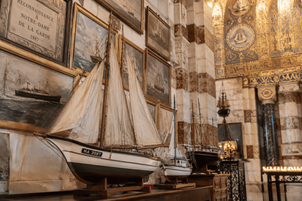 Des maquettes de voiliers et des tableaux maritimes sont exposés devant des mosaïques et des murs de marbre dans la basilique.