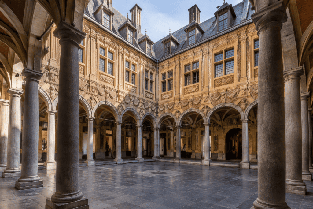Cour intérieure pavée entourée de galeries à arcades et de façades richement décorées.