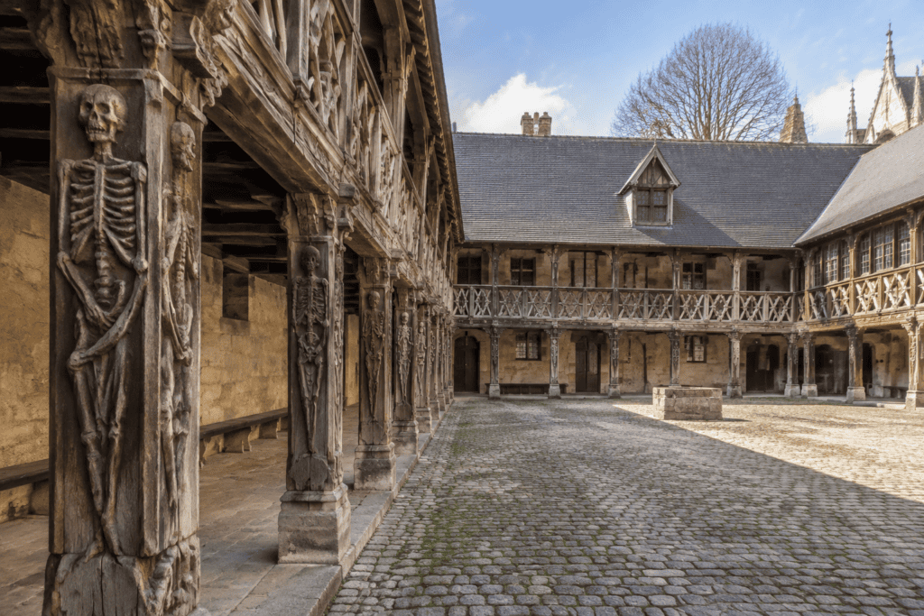 Cour pavée bordée de galeries à pans de bois, avec une sculpture de squelette sur un poteau.