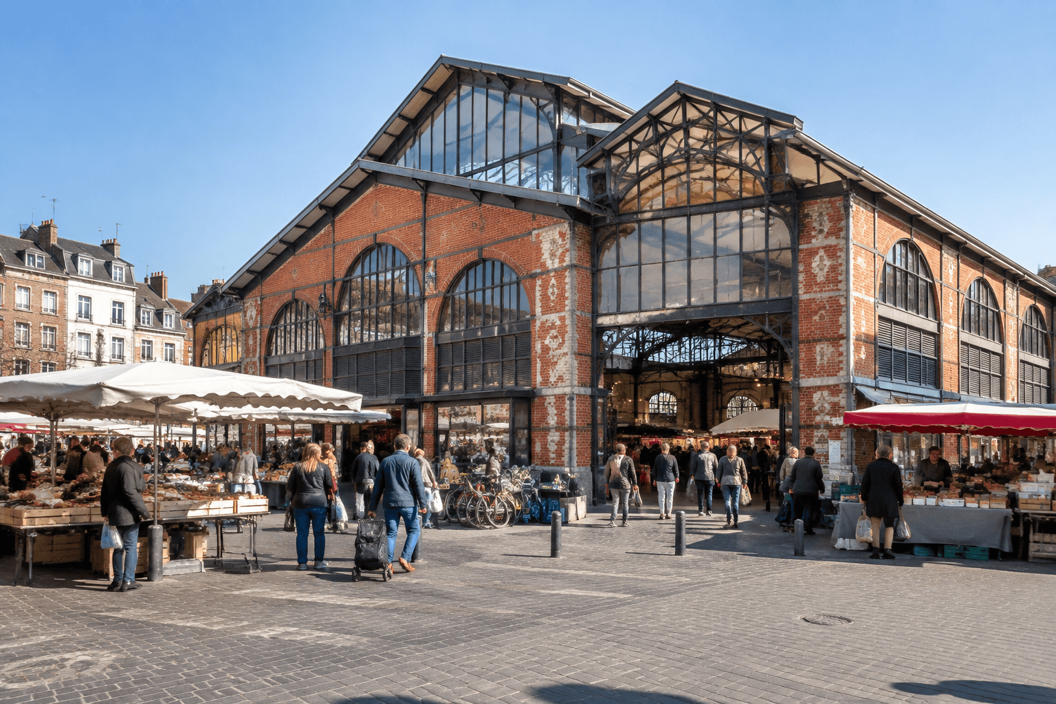 Grande halle en brique rouge et en verre, avec des étals et des visiteurs sur la place devant le bâtiment.