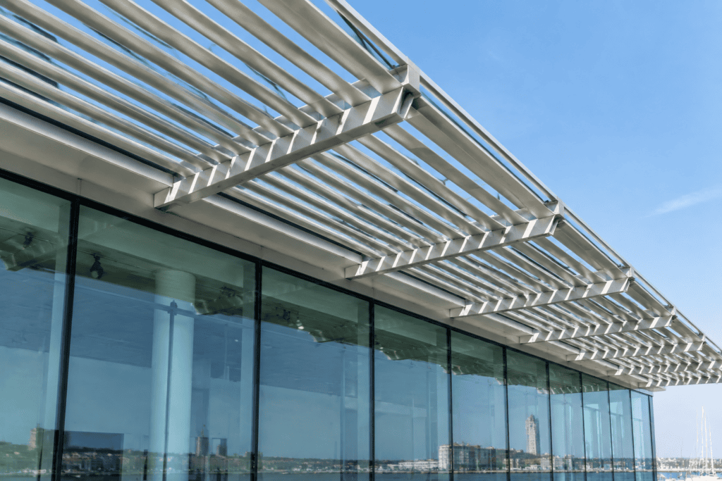 Des lames métalliques inclinées surplombent la façade vitrée du MuMa, avec le front de mer visible dans les reflets.