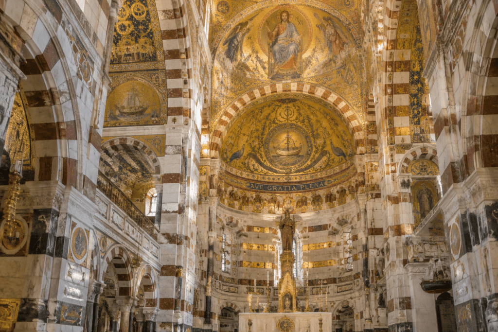 L’intérieur de la basilique présente des mosaïques dorées, des arcs en pierre claire et foncée et un sanctuaire au fond de l’église.