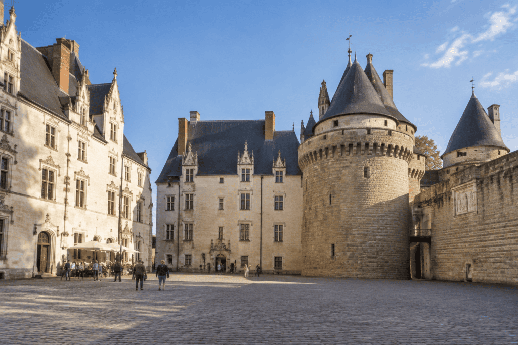 Cour pavée entourée de bâtiments de pierre et de tours rondes au château des ducs de Bretagne.