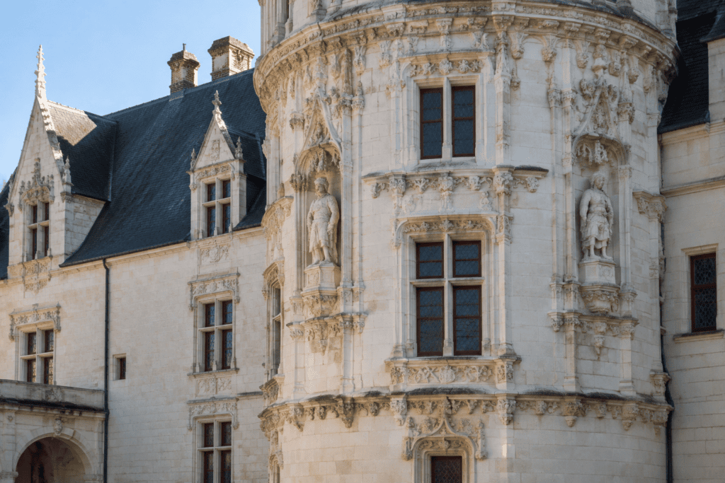 Tour arrondie en pierre claire ornée de sculptures en niches et de fenêtres, avec les façades du château à Nantes.