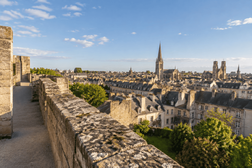 Un chemin de rempart en pierre domine les toits et les clochers du centre de Caen.