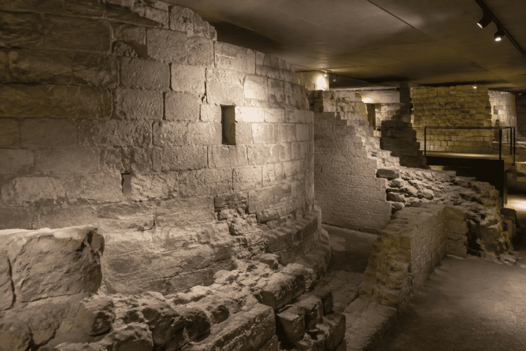 Murs de pierre anciens et vestiges de maçonnerie dans un espace souterrain éclairé.