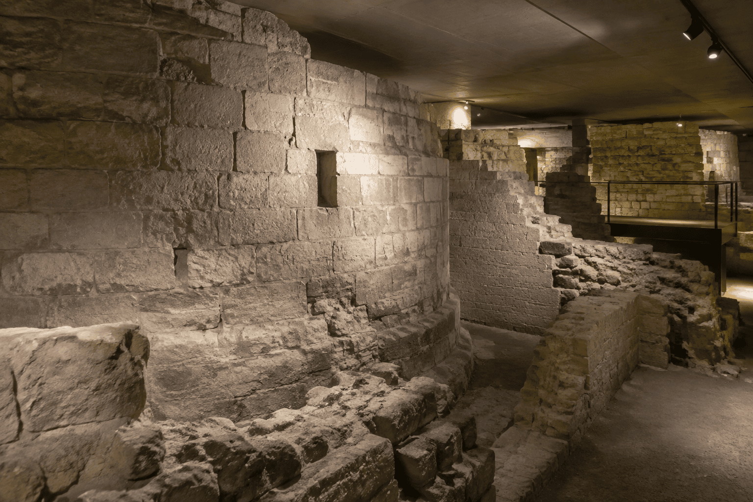 Murs de pierre anciens et vestiges de maçonnerie dans un espace souterrain éclairé.