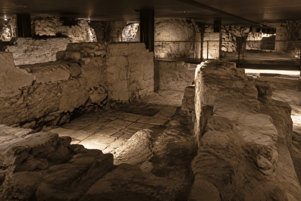 Murs et fondations en pierre ancienne dans un espace souterrain éclairé par endroits.