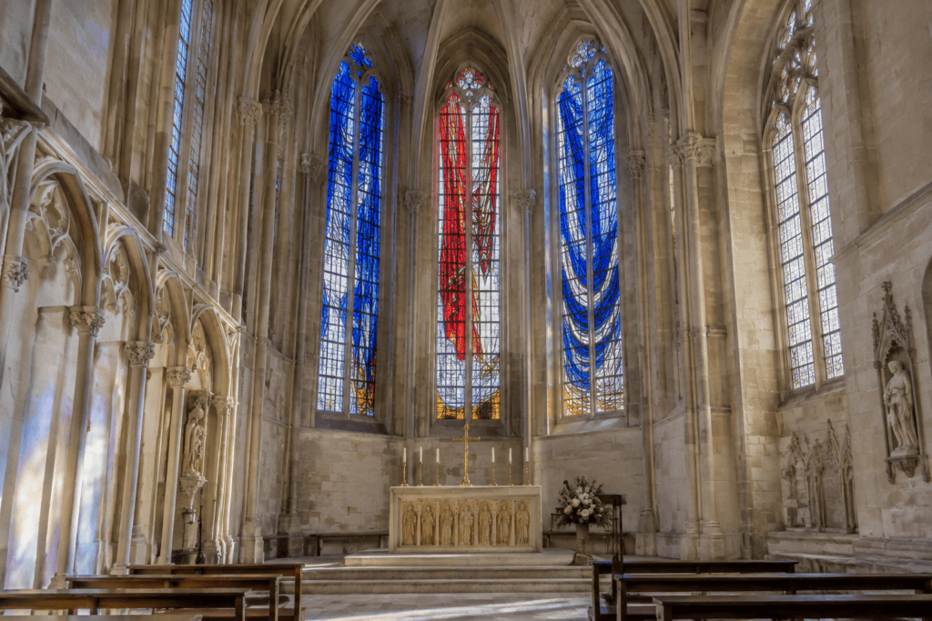 Dans une chapelle aux voûtes gothiques, de grands vitraux bleus et rouges éclairent l’autel et les bancs.