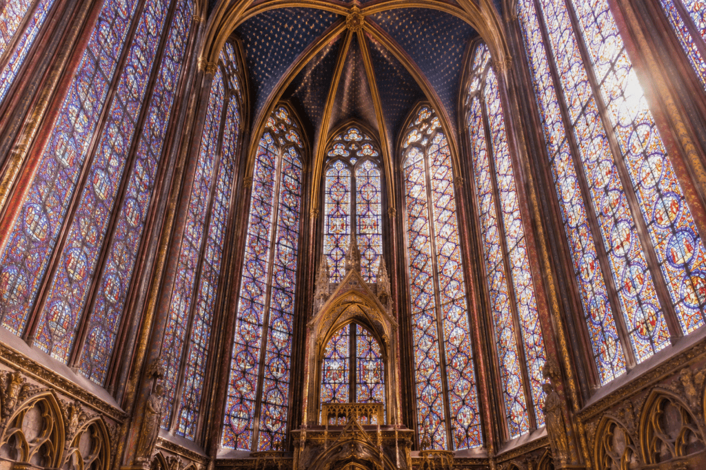 De hautes verrières colorées s’élèvent sous une voûte gothique ornée.