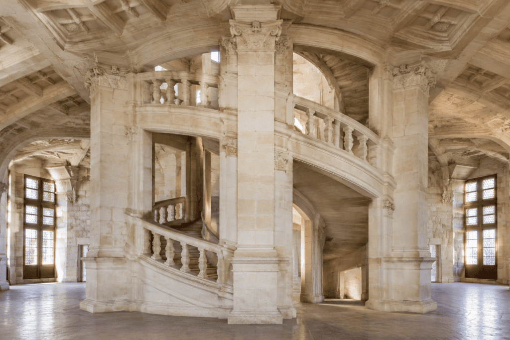 Grand escalier de pierre à deux volées en spirale dans une salle voûtée.