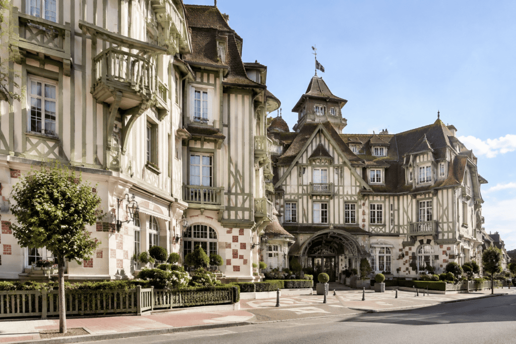 Façade à colombages de l’Hôtel Barrière Le Normandy, avec une entrée en arc et une rue au premier plan.