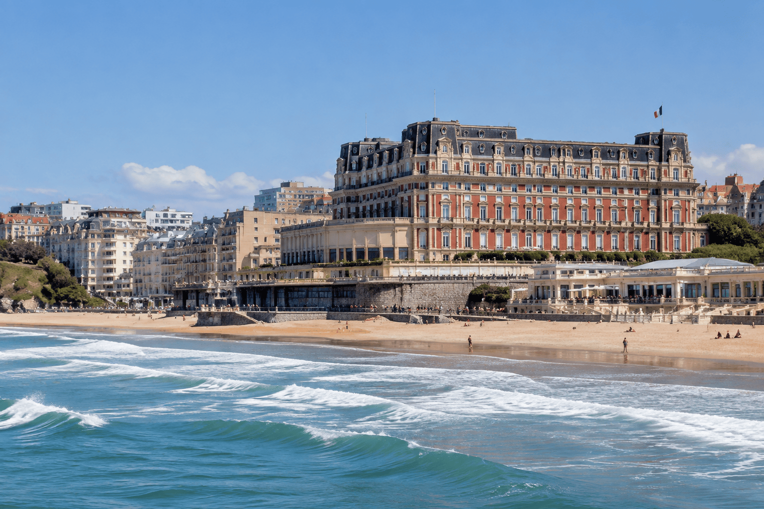 Façade de l’Hôtel du Palais dominant une plage de Biarritz, avec les vagues au premier plan.