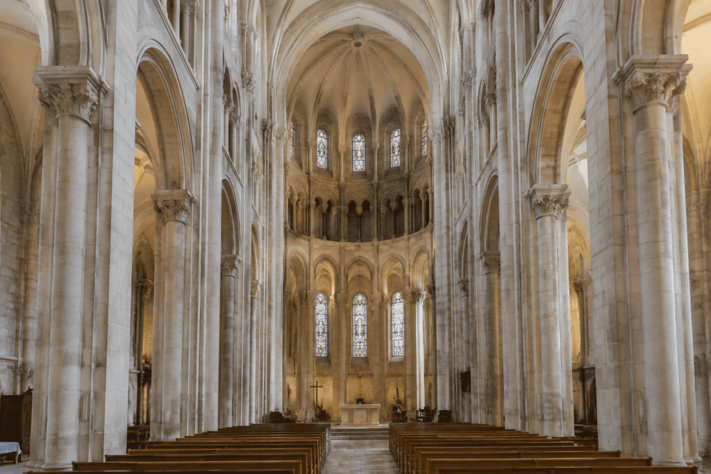 Vue axiale d’une nef en pierre, avec des rangées de bancs, de hauts piliers et des voûtes.