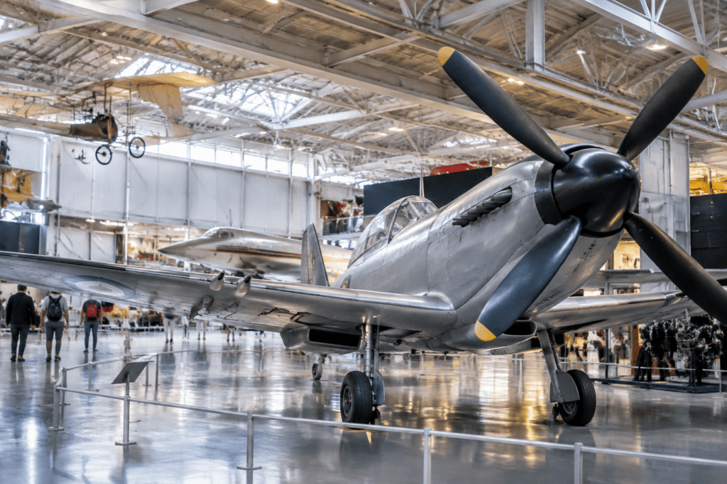 Avion à hélice exposé dans une grande galerie, avec d’autres appareils visibles en arrière-plan.