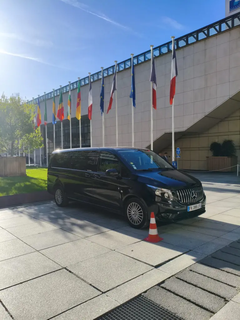 Van Mercedes noir devant un bâtiment bordé de drapeaux