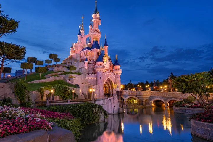 Le château de Disneyland Paris éclairé au bord de son plan d’eau